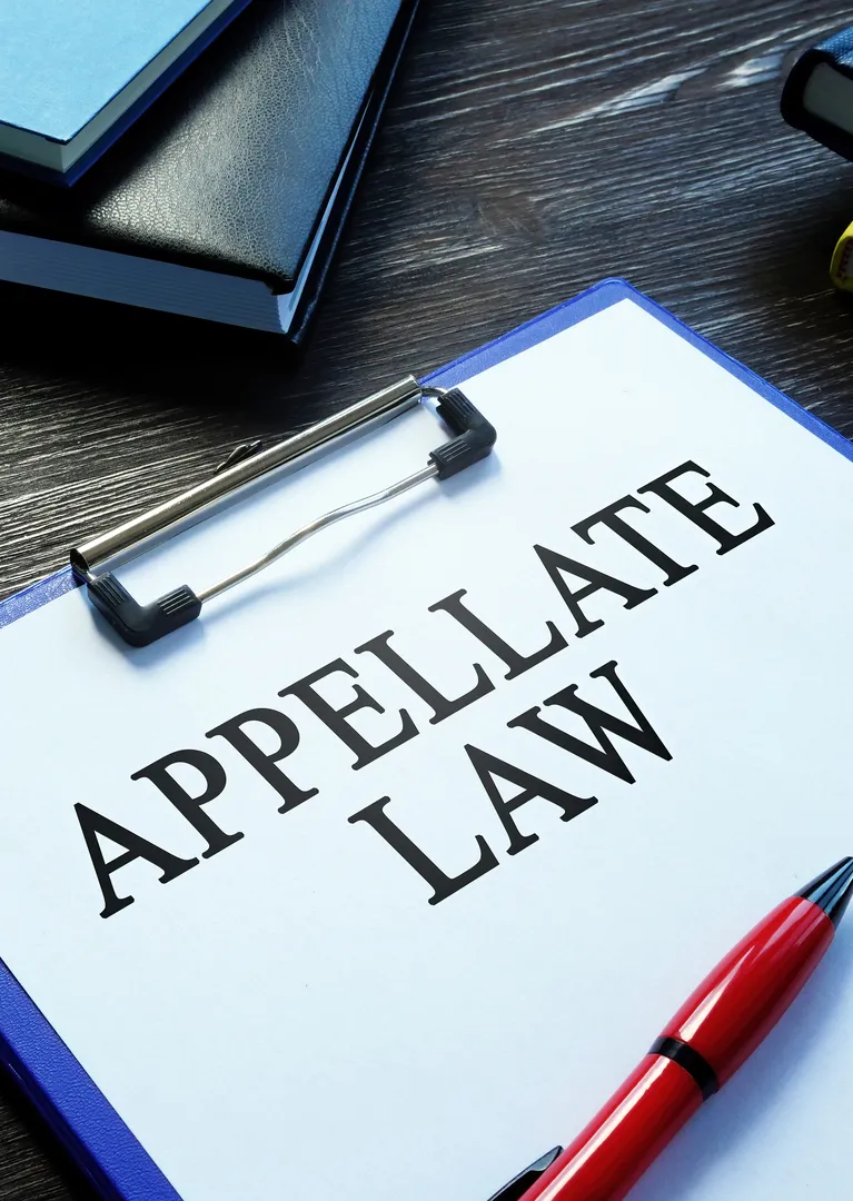 Clipboard with document titled "APPELLATE LAW" on a dark wooden desk, next to a red pen and closed black books.