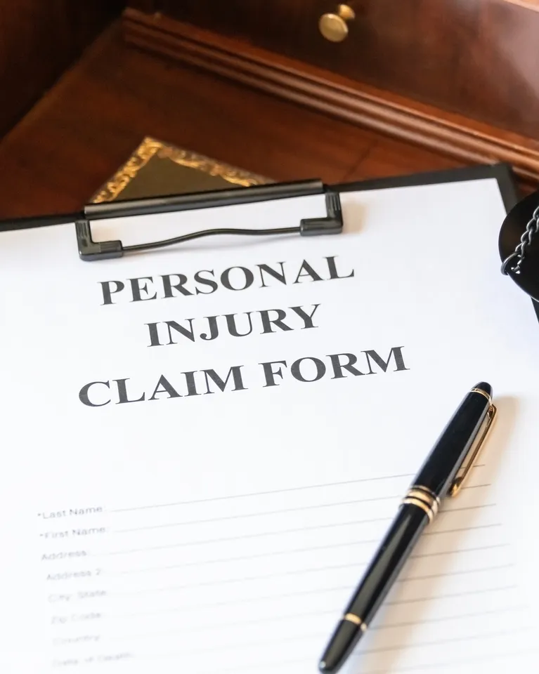 Personal injury claim form on clipboard with black and gold pen on wooden desk.