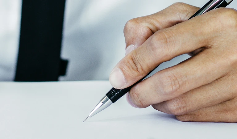 Close-up of a hand holding a mechanical pencil poised above a blank white sheet.