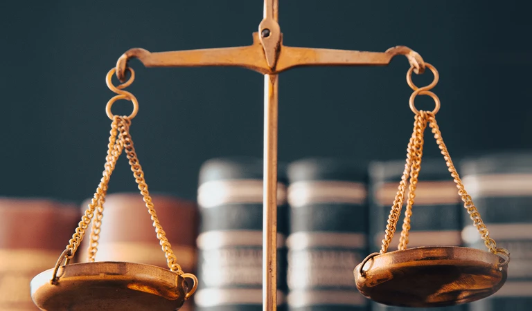 Close-up of a golden balance scale with blurred law books in the background.