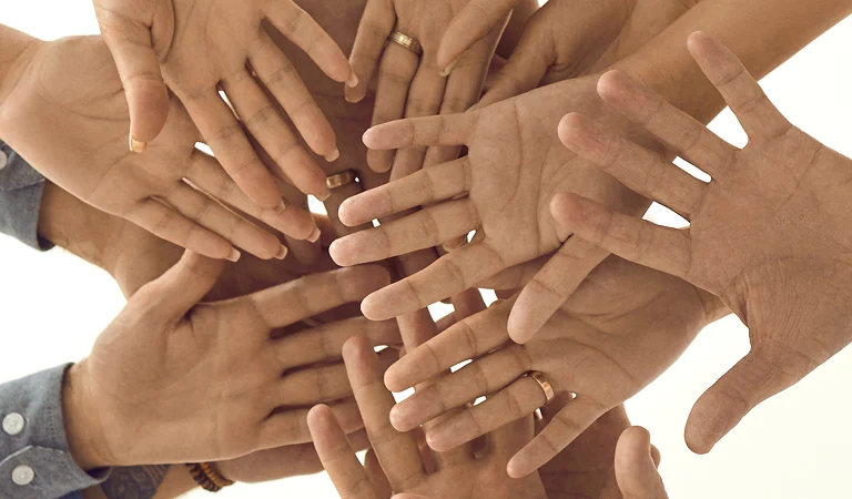 Multiple diverse hands joined together in a circle against a light background.